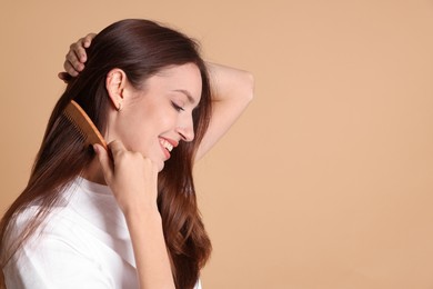 Photo of Smiling woman brushing her hair with comb on beige background, space for text