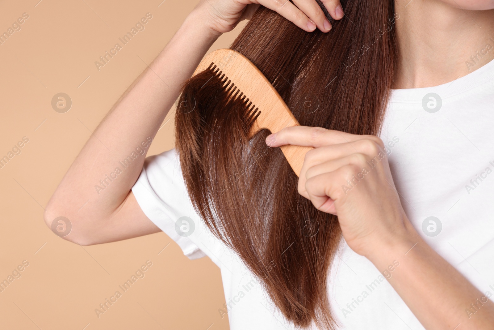 Photo of Woman brushing her hair with comb on beige background, closeup