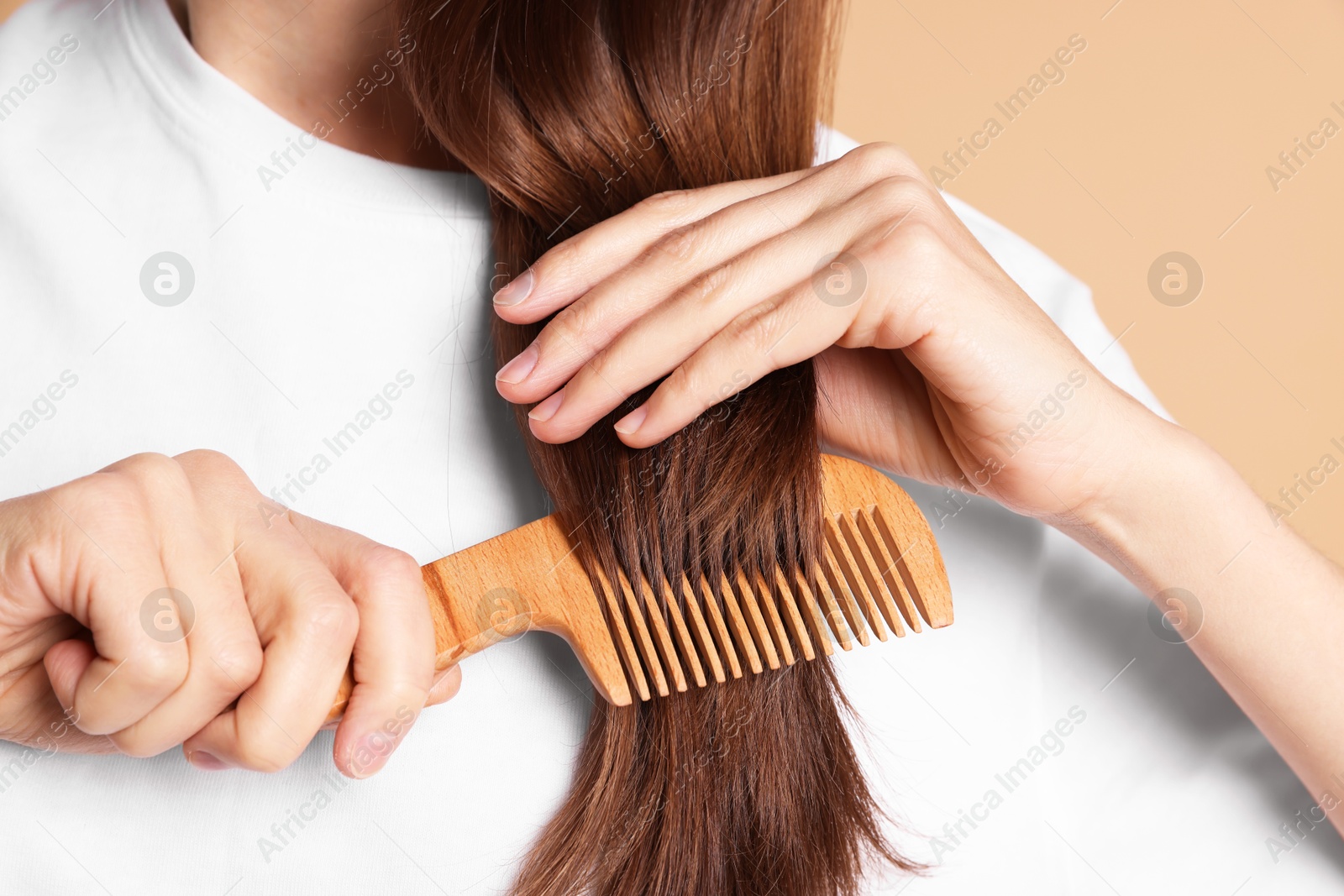 Photo of Woman brushing her hair with comb on beige background, closeup