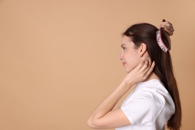 Beautiful woman brushing her hair on beige background, space for text