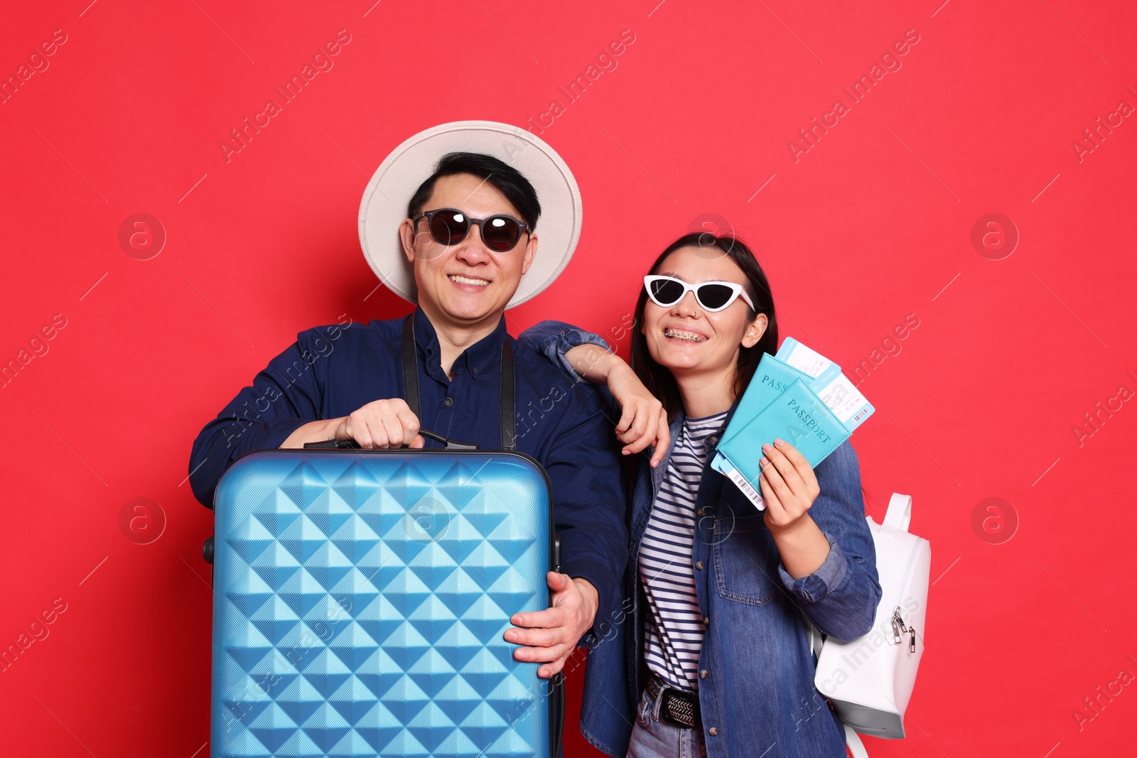 Photo of Happy travellers with passports and suitcase on red background