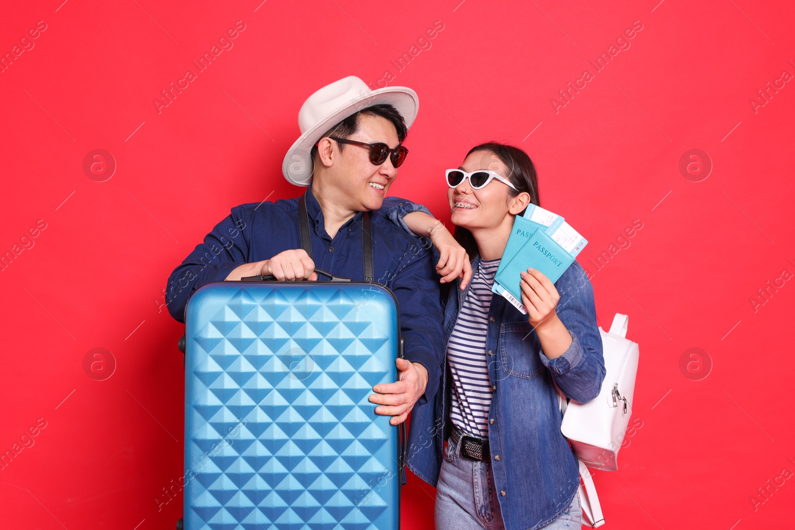 Photo of Happy travellers with passports and suitcase on red background