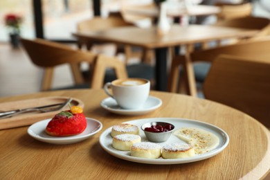 Photo of Delicious cottage cheese pancakes, dessert and coffee served on wooden table in cafe