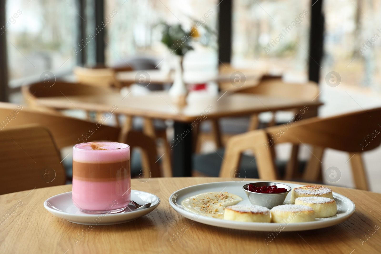 Photo of Delicious cottage cheese pancakes and pink latte served on wooden table indoors