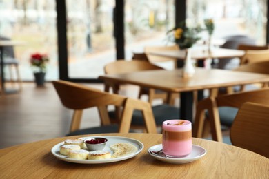 Photo of Delicious cottage cheese pancakes and pink latte served on wooden table indoors