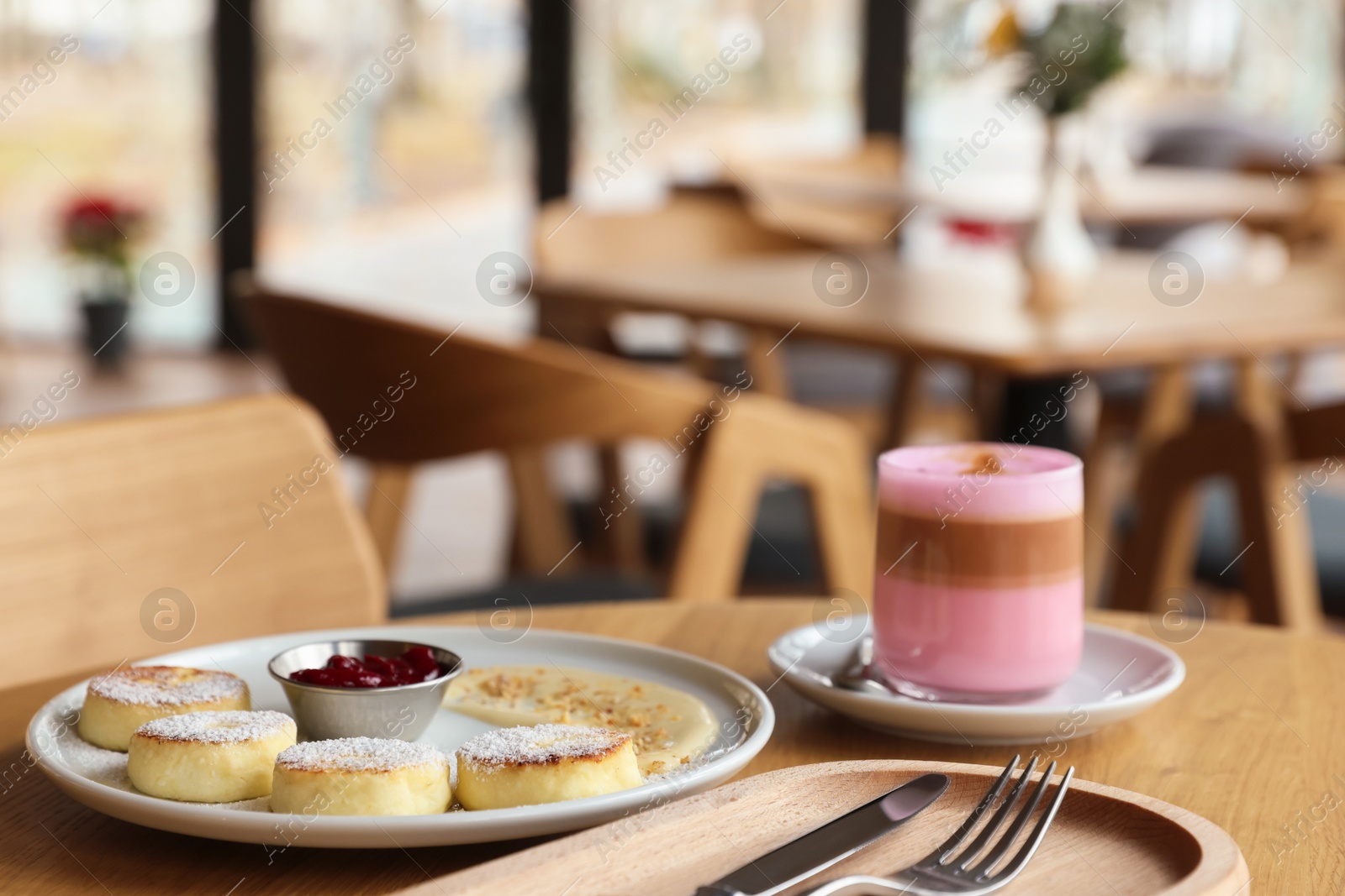 Photo of Delicious cottage cheese pancakes and pink latte served on wooden table indoors