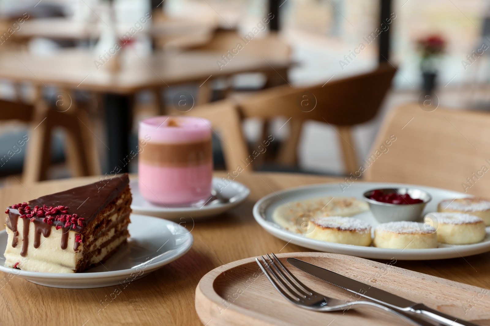 Photo of Delicious cottage cheese pancakes, cake and coffee served on wooden table in cafe