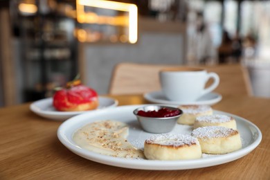 Photo of Delicious cottage cheese pancakes, dessert and coffee served on wooden table in cafe, closeup