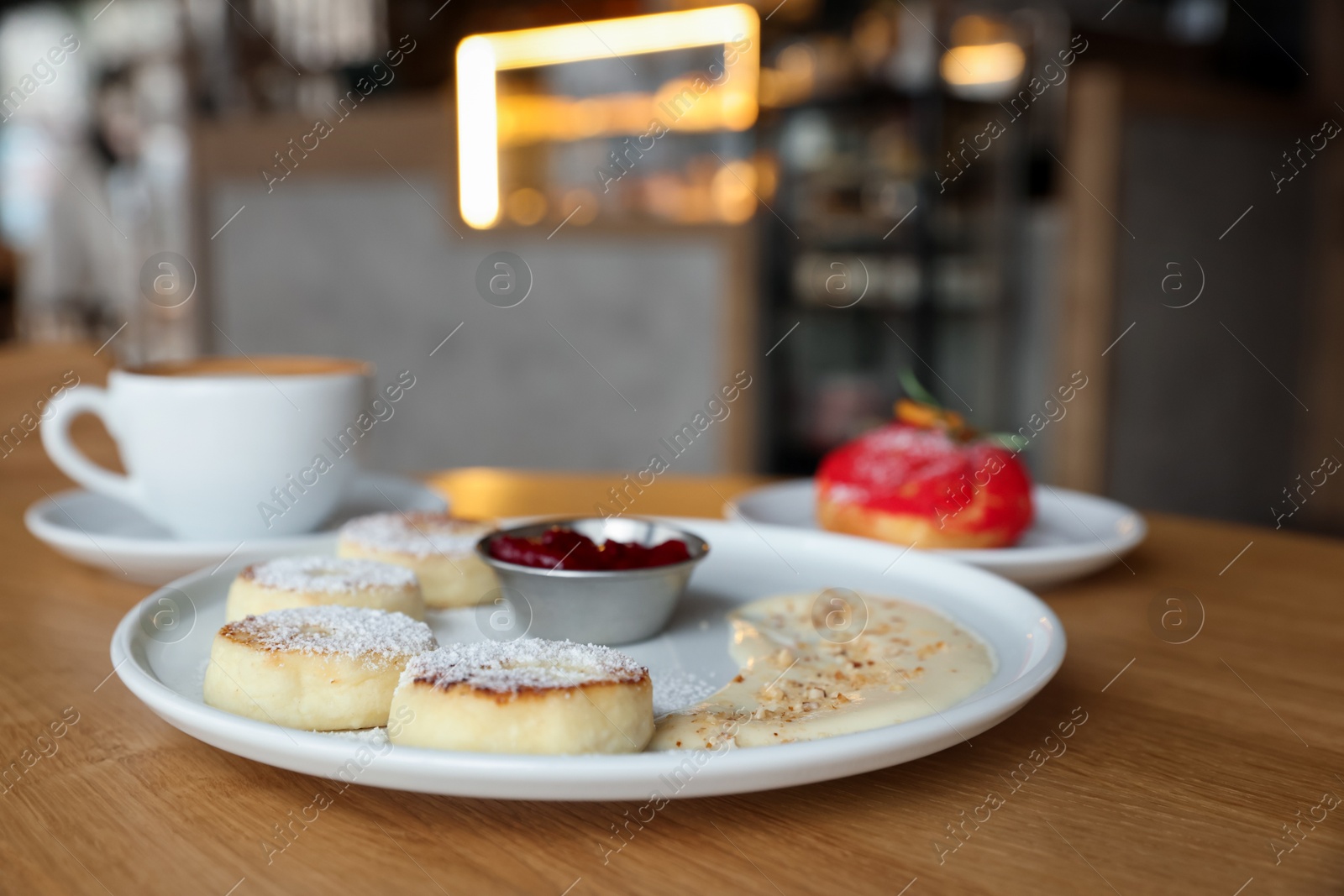 Photo of Delicious cottage cheese pancakes, dessert and coffee served on wooden table in cafe, closeup