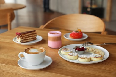 Photo of Delicious cottage cheese pancakes, desserts and aromatic coffee served on wooden table in cafe