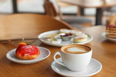 Photo of Aromatic coffee and delicious desserts served on wooden table in cafe