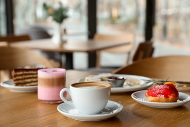 Photo of Aromatic coffee and delicious desserts served on wooden table in cafe