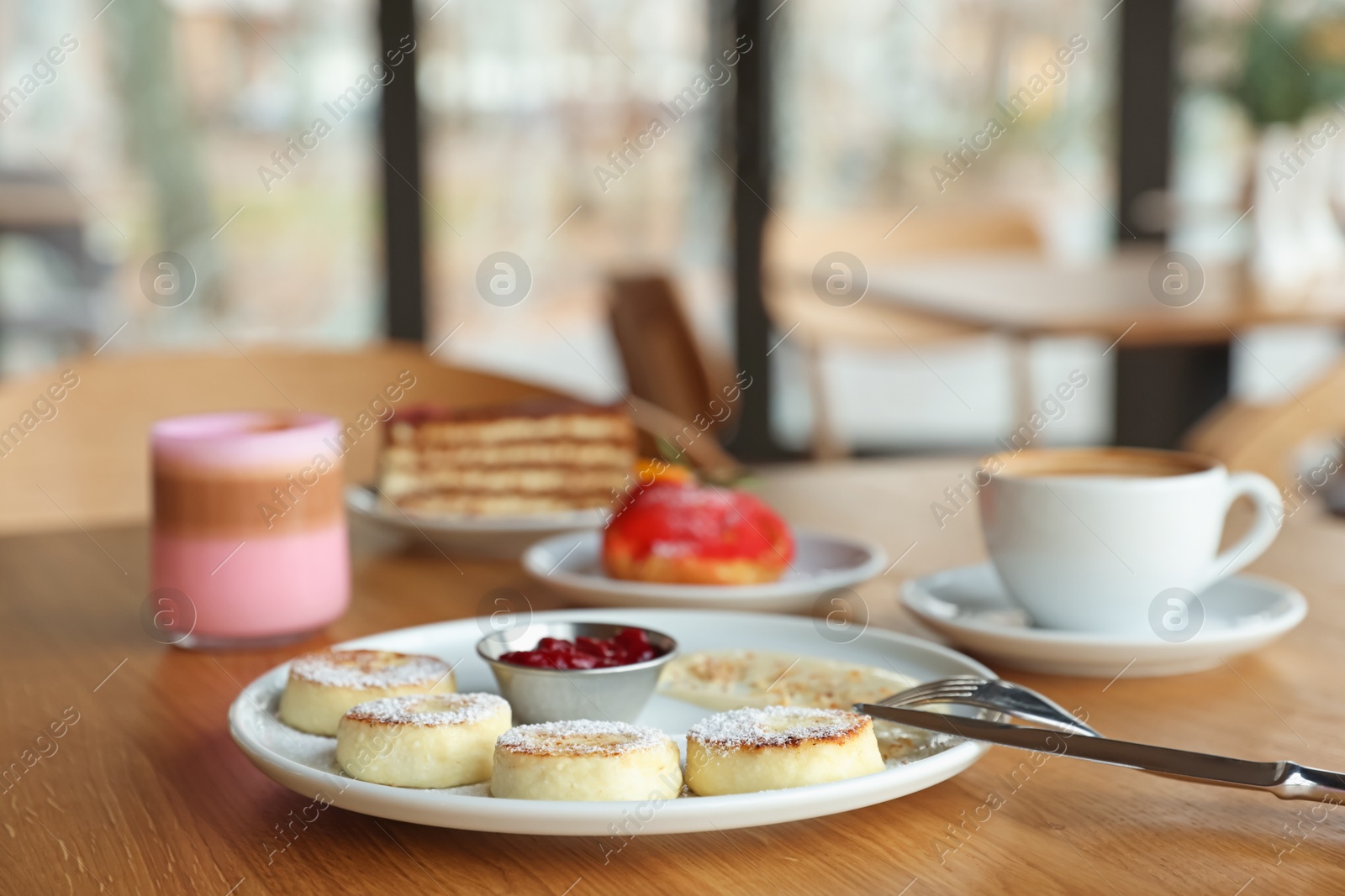 Photo of Delicious cottage cheese pancakes, desserts and aromatic coffee served on wooden table in cafe