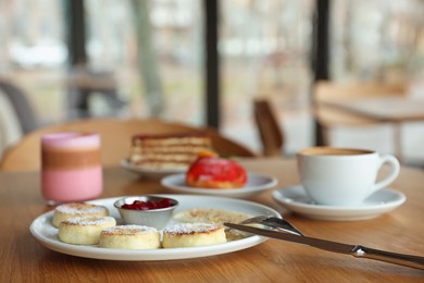 Photo of Delicious cottage cheese pancakes, desserts and aromatic coffee served on wooden table in cafe