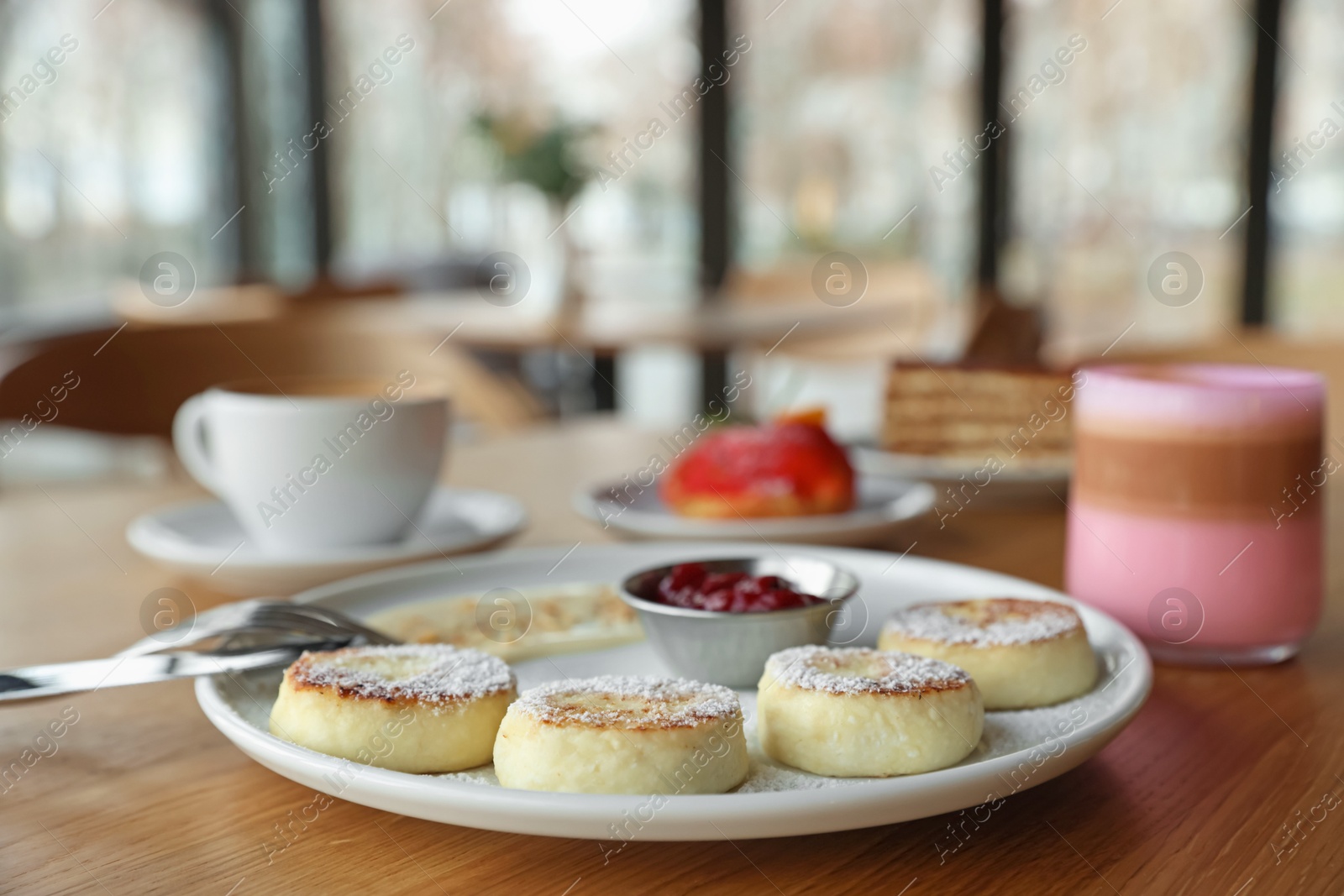 Photo of Delicious cottage cheese pancakes, desserts and aromatic coffee served on wooden table in cafe, closeup