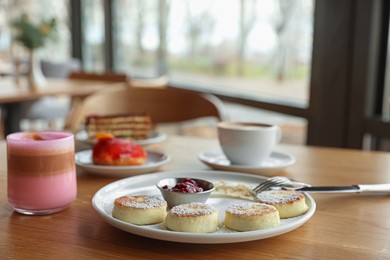 Photo of Delicious cottage cheese pancakes, desserts and aromatic coffee served on wooden table in cafe