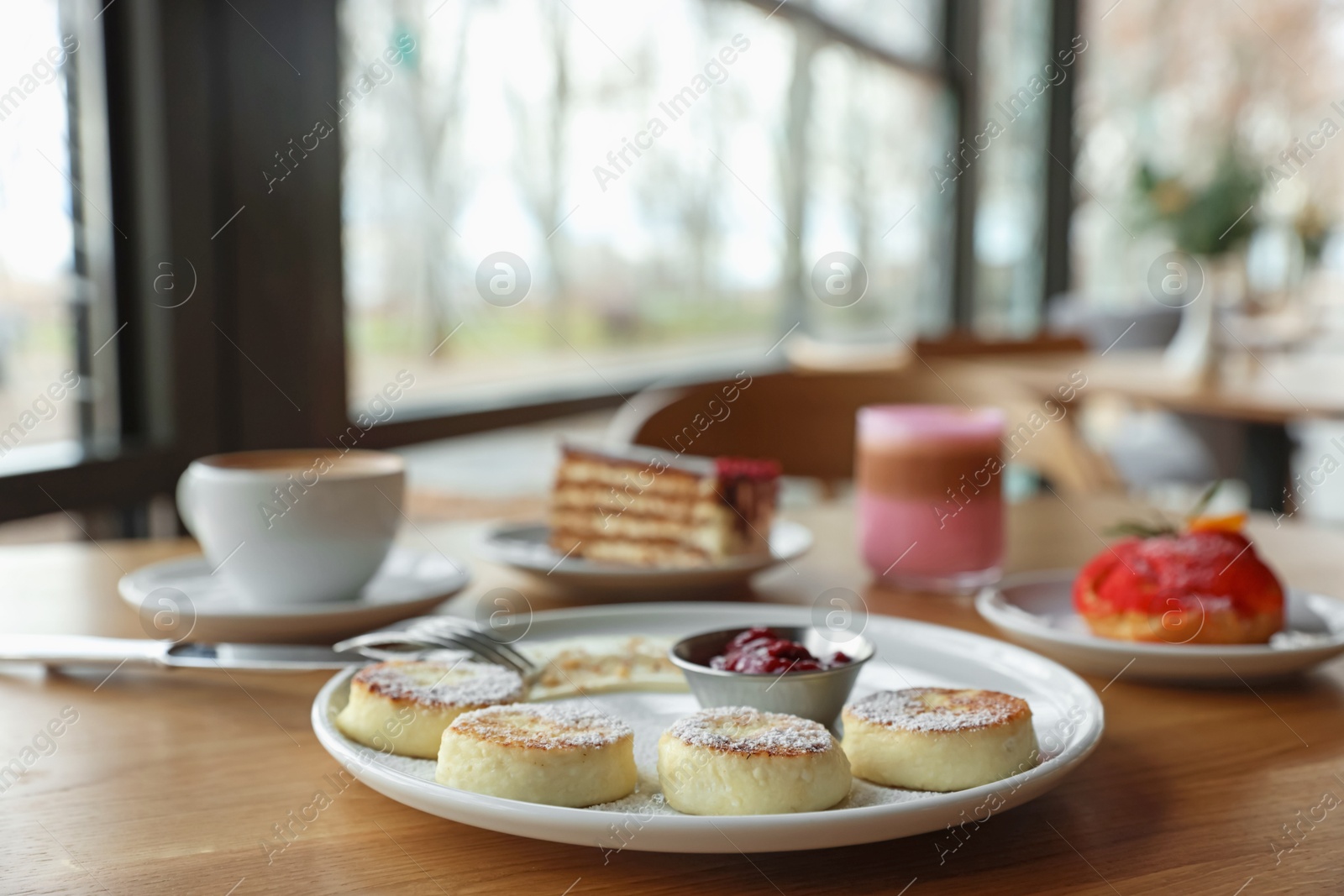 Photo of Delicious cottage cheese pancakes, desserts and aromatic coffee served on wooden table in cafe