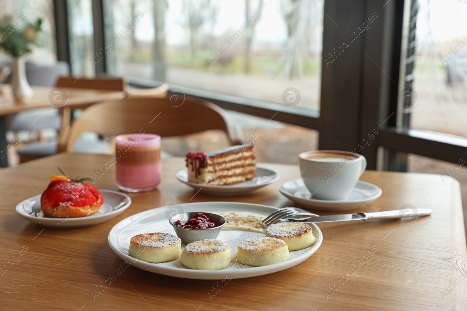 Photo of Delicious cottage cheese pancakes, desserts and aromatic coffee served on wooden table in cafe