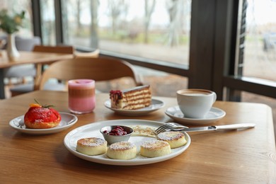 Photo of Delicious cottage cheese pancakes, desserts and aromatic coffee served on wooden table in cafe