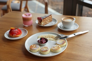 Photo of Delicious cottage cheese pancakes, desserts and aromatic coffee served on wooden table in cafe