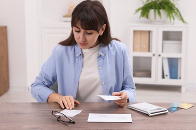 Photo of Paying bills. Woman with different invoices and calculator at wooden table indoors