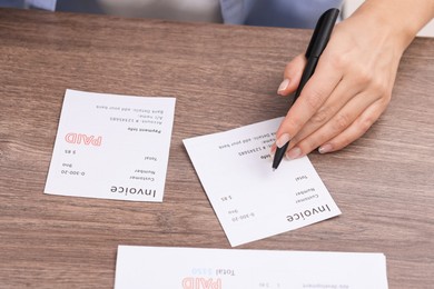 Photo of Paying bills. Woman with different invoices at wooden table indoors, closeup