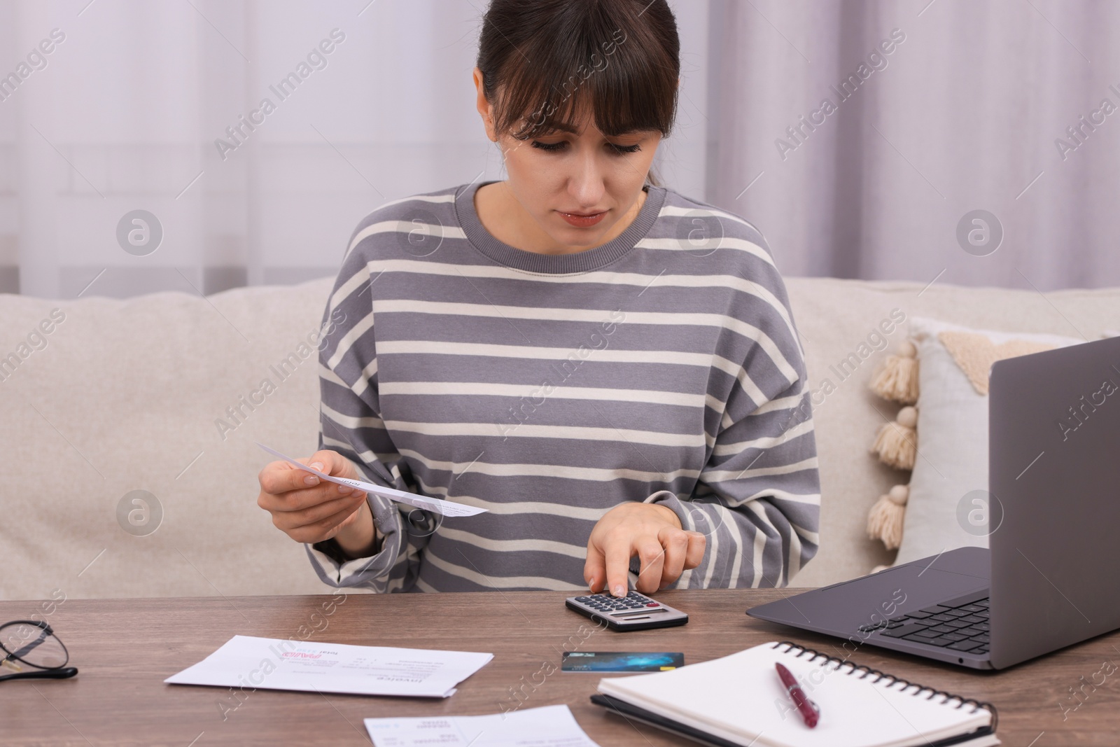 Photo of Paying bills. Woman with different invoices and calculator at wooden table indoors