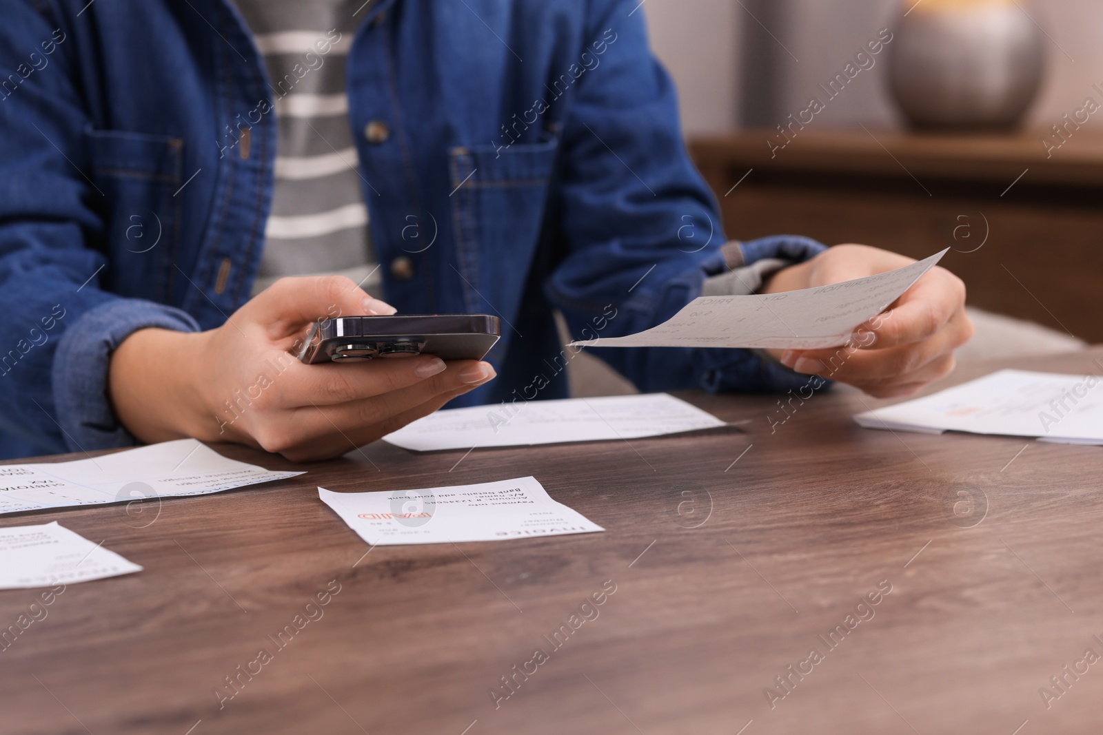 Photo of Paying bills. Woman with different invoices and phone at wooden table indoors, closeup