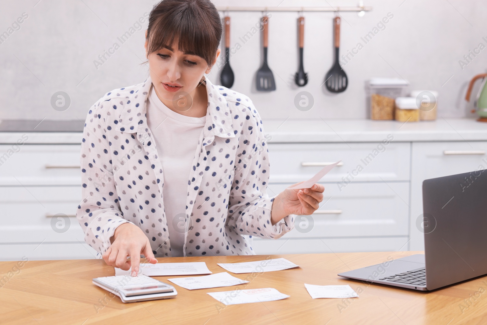 Photo of Paying bills. Woman with different invoices and calculator at wooden table indoors