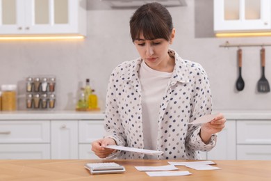 Photo of Paying bills. Woman with different invoices and calculator at wooden table indoors