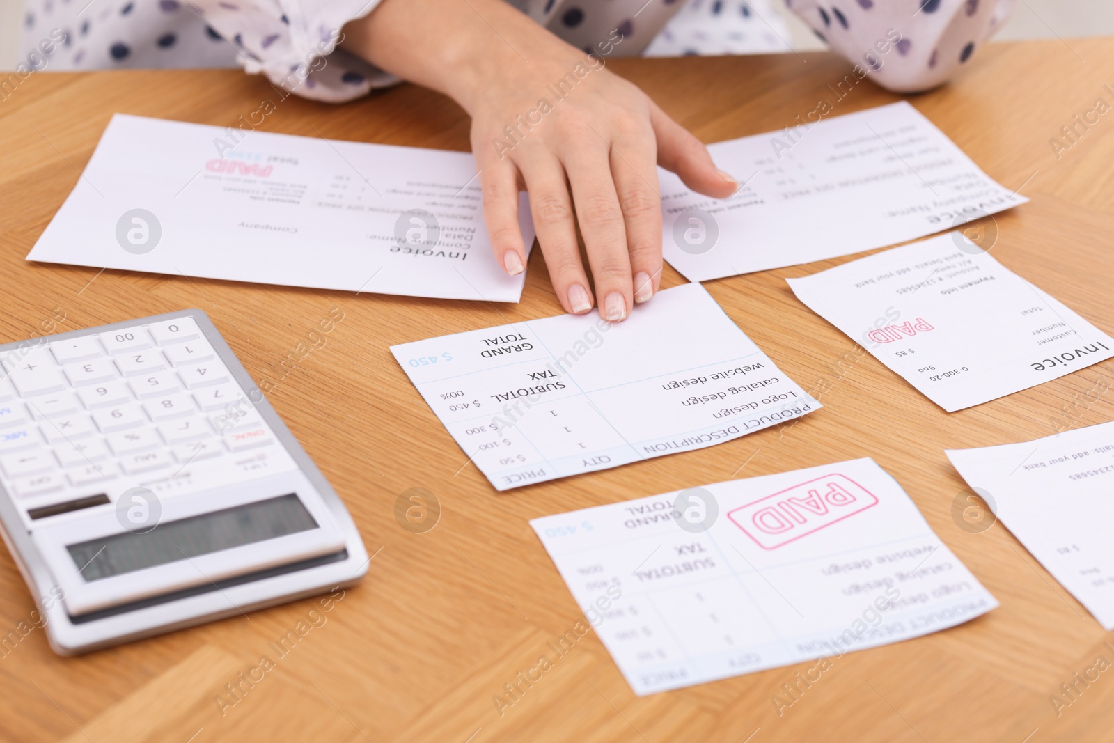 Photo of Paying bills. Woman with different invoices and calculator at wooden table indoors, closeup