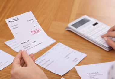 Photo of Paying bills. Woman with different invoices and calculator at wooden table indoors, closeup