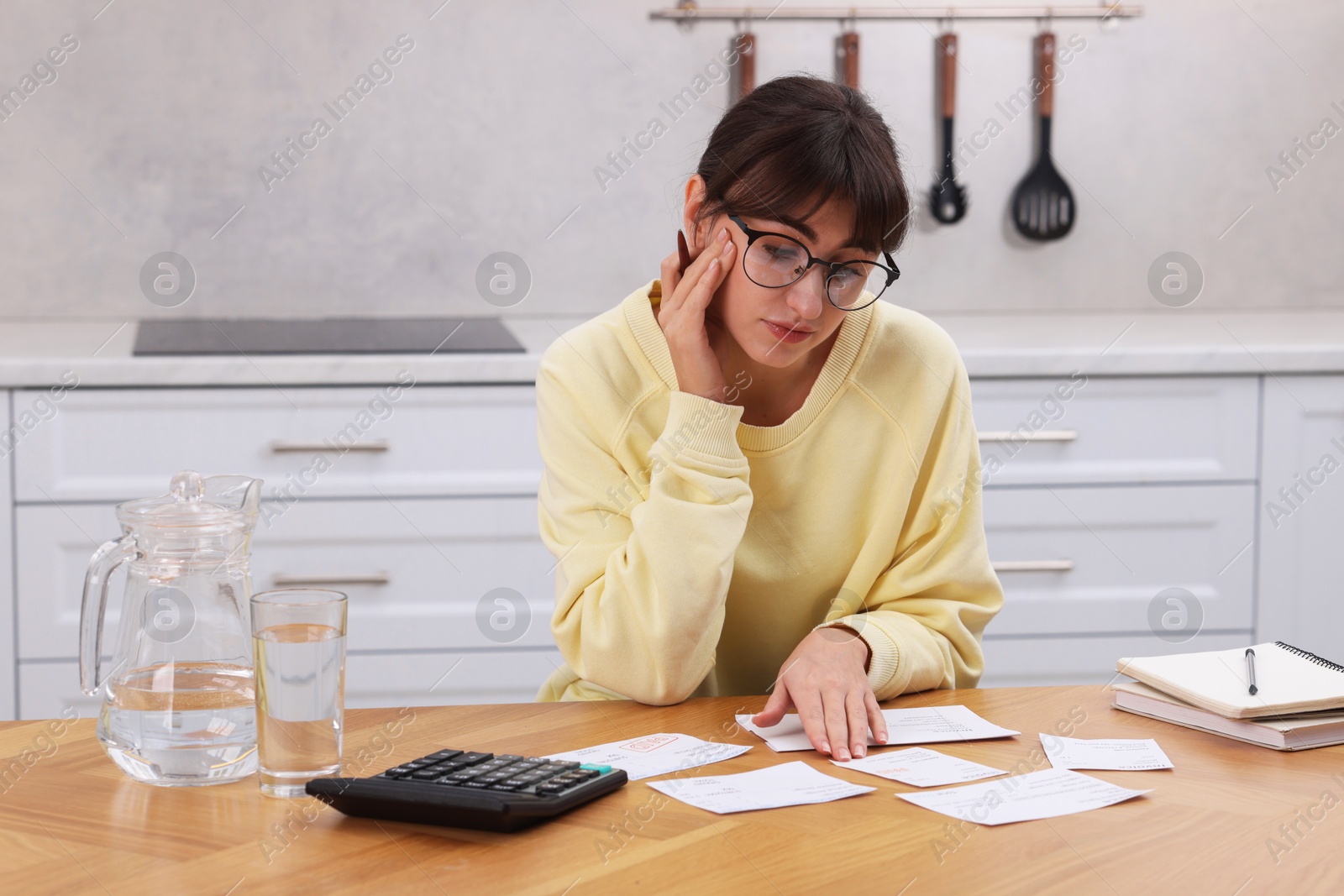 Photo of Paying bills. Upset woman with different invoices and calculator at wooden table indoors