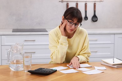 Photo of Paying bills. Upset woman with different invoices and calculator at wooden table indoors