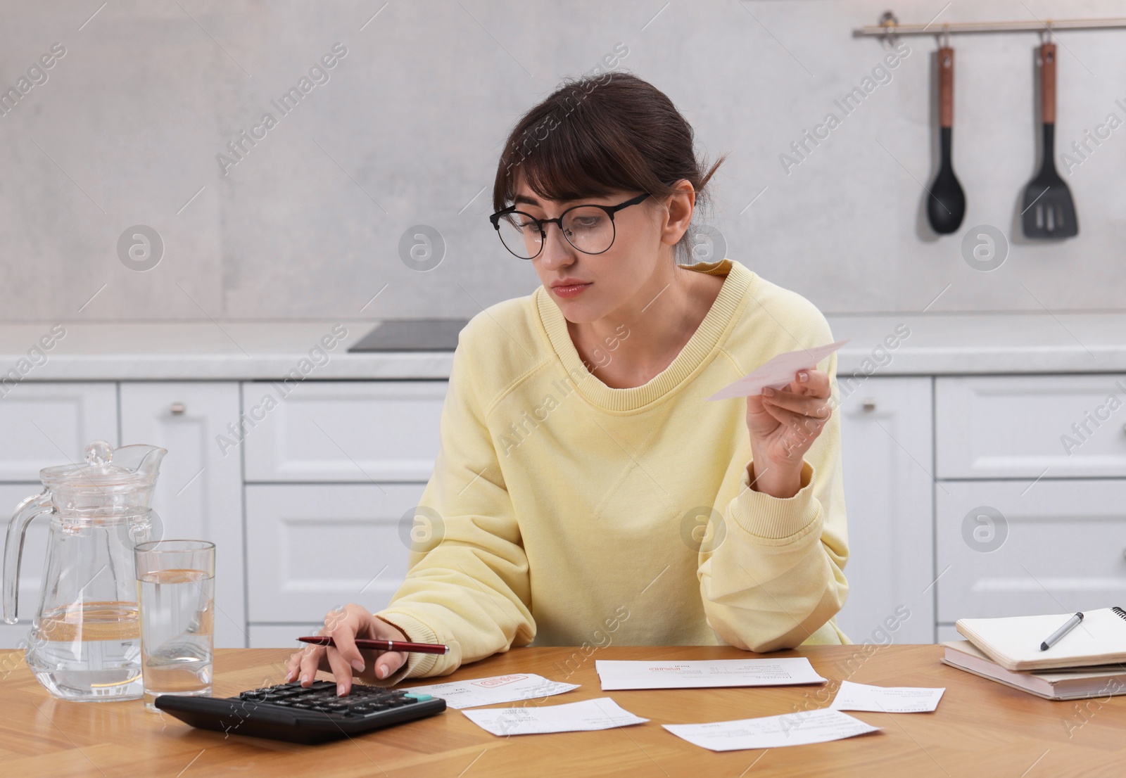 Photo of Paying bills. Woman with different invoices and calculator at wooden table indoors