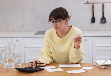 Photo of Paying bills. Woman with different invoices and calculator at wooden table indoors