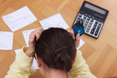 Photo of Paying bills. Woman with different invoices, credit card and calculator at wooden table indoors, top view