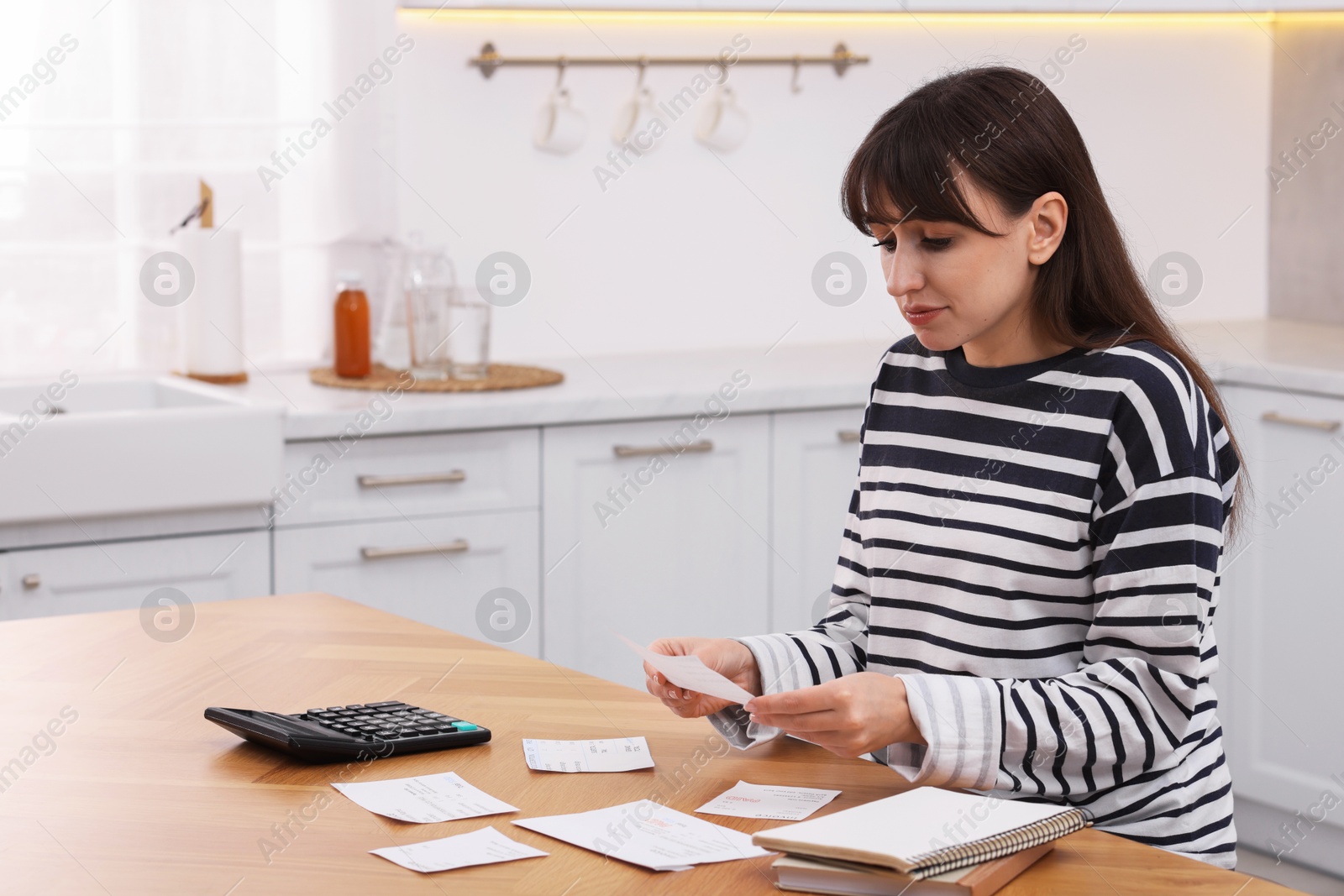 Photo of Paying bills. Woman with different invoices and calculator at wooden table indoors