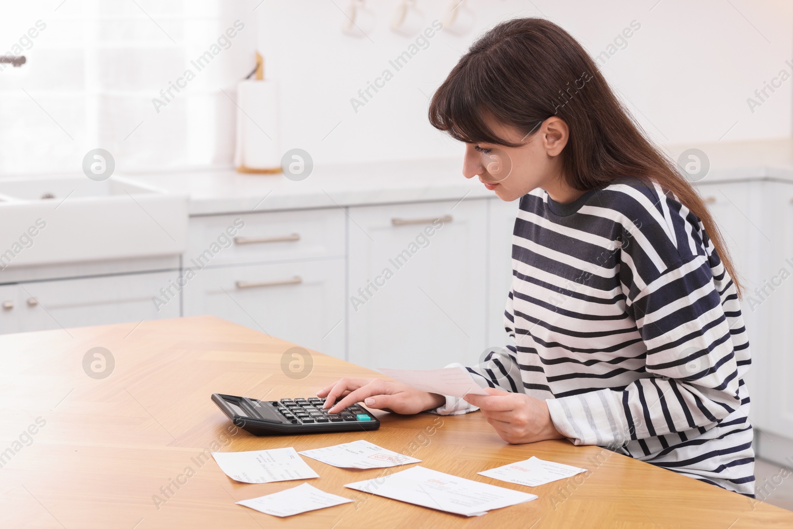 Photo of Paying bills. Woman with different invoices and calculator at wooden table indoors, space for text