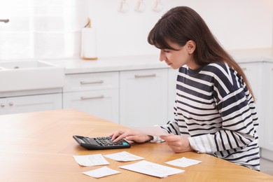 Photo of Paying bills. Woman with different invoices and calculator at wooden table indoors, space for text