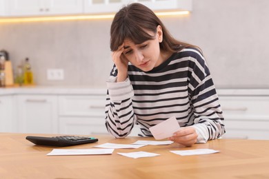 Photo of Paying bills. Upset woman with different invoices and calculator at wooden table indoors