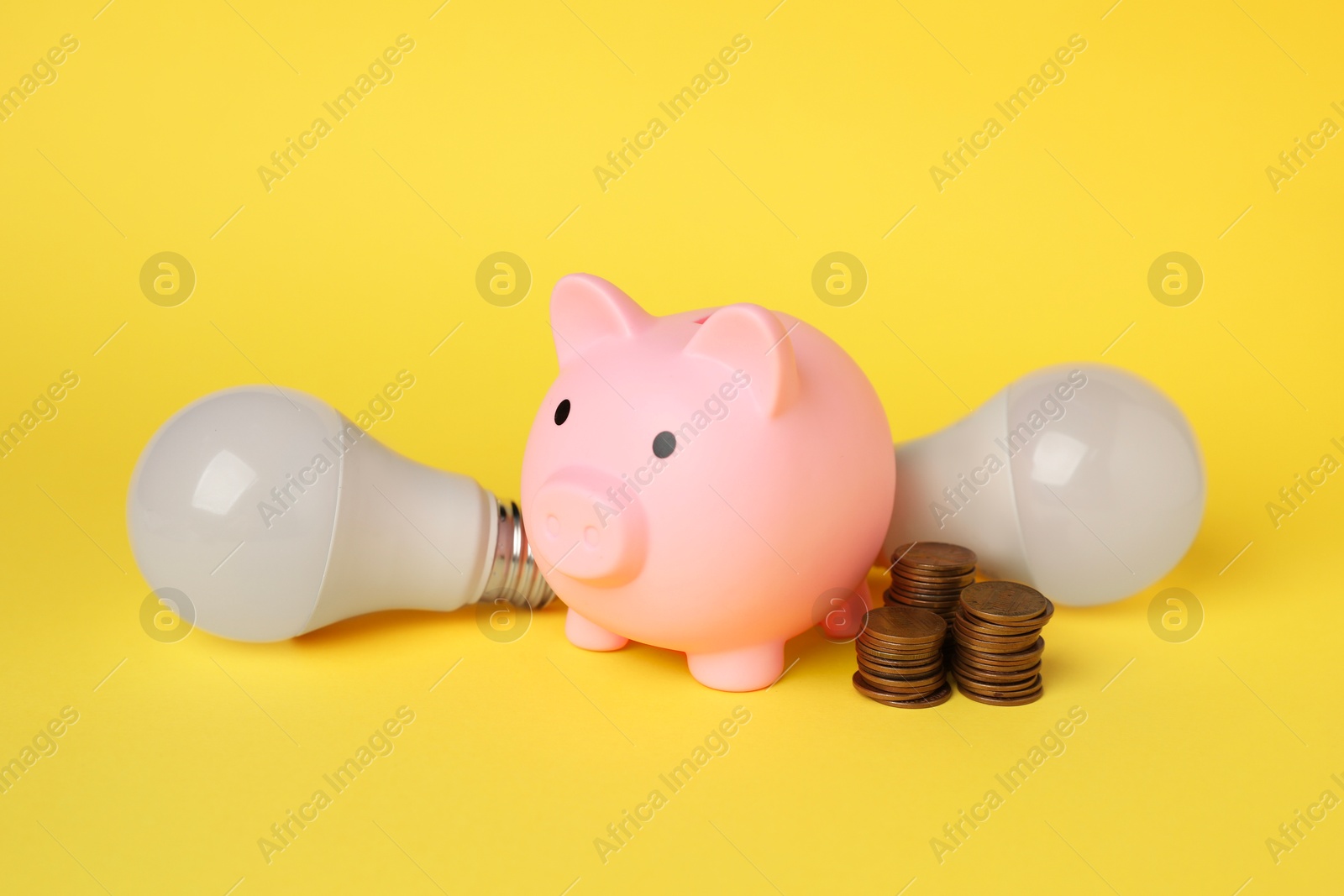 Photo of Piggy bank, coins and light bulbs on yellow background. Energy saving concept