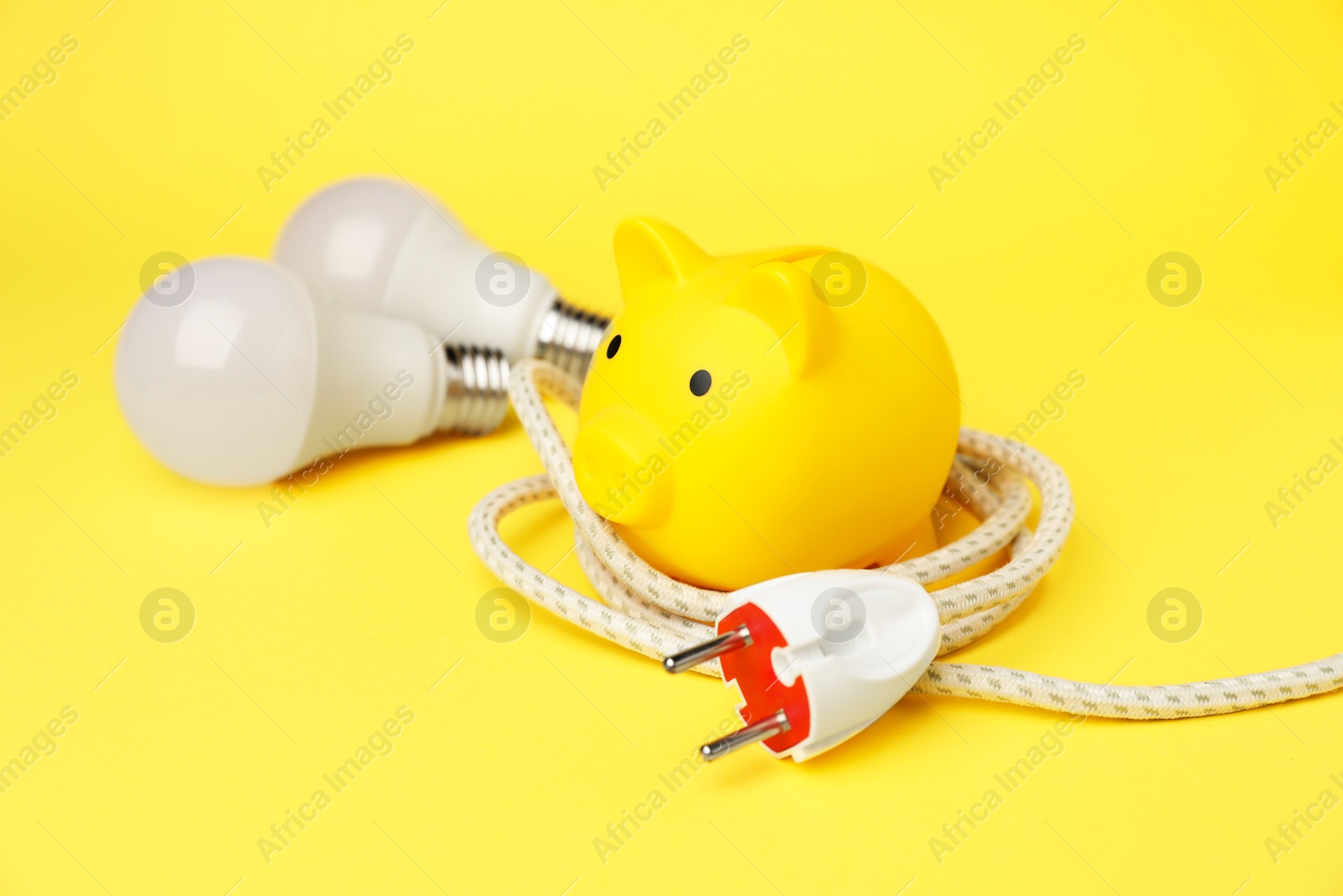 Photo of Piggy bank, light bulbs and plug on yellow background. Energy saving concept