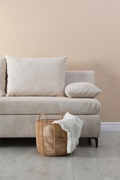 Photo of Comfortable sofa with pillows and basket near beige wall