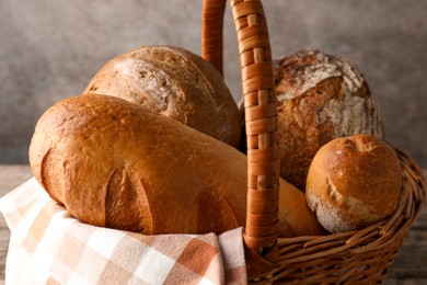 Photo of Different freshly baked bread loafs in wicker basket on table, closeup