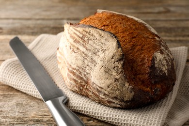 Photo of Freshly baked bread and knife on wooden table, closeup