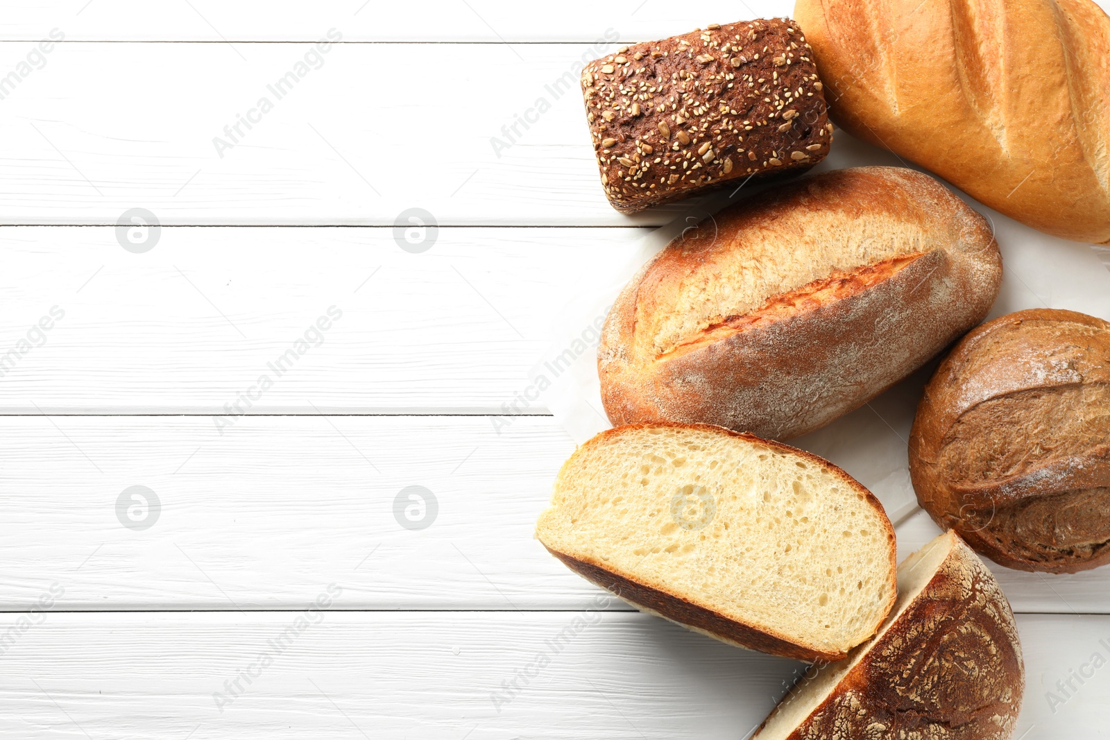 Photo of Whole and cut bread loafs on white wooden table, flat lay. Space for text