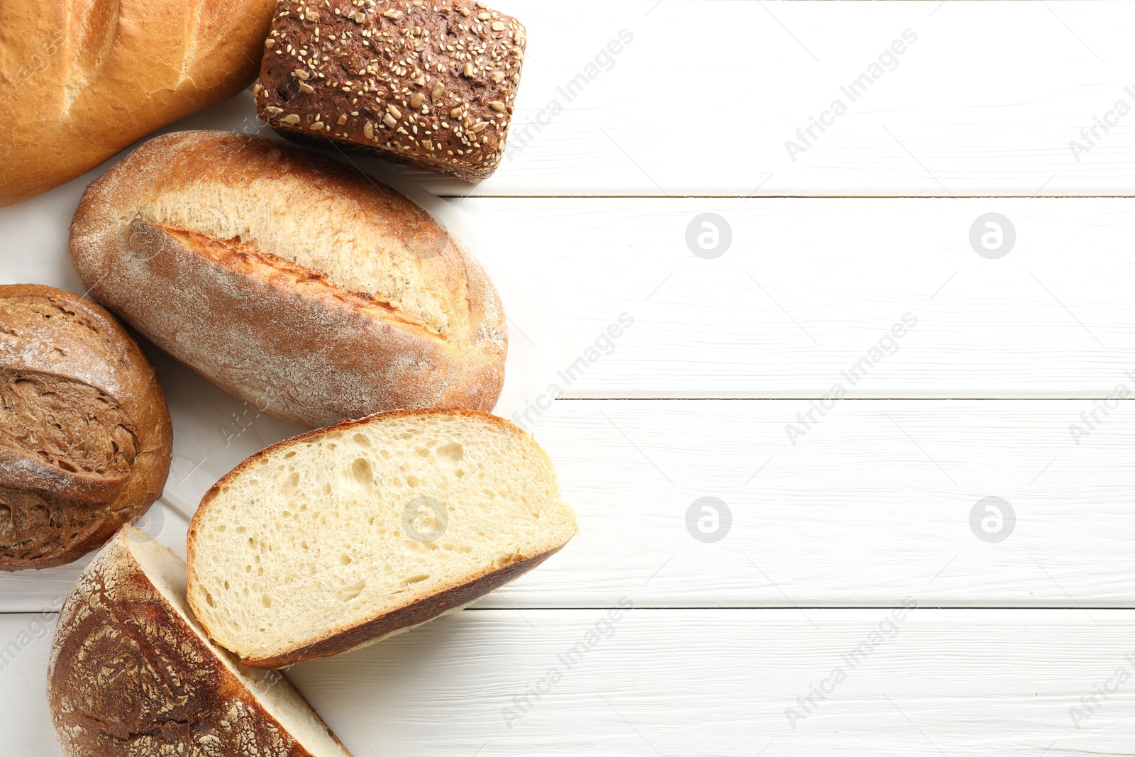 Photo of Whole and cut bread loafs on white wooden table, flat lay. Space for text