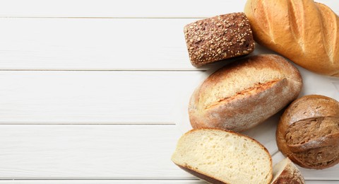 Photo of Whole and cut bread loafs on white wooden table, flat lay. Space for text