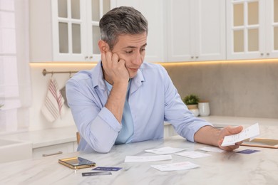 Photo of Paying bills. Man with reviewing invoices at white marble table indoors